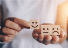 een hand neemt een blokje met lachtend gezicht vast, in de andere hand blijven de blokjes met vlak en droef gezicht liggen